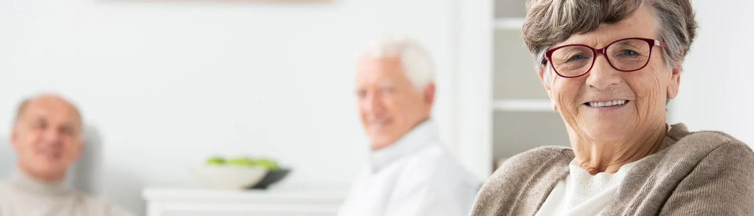 Lächelnde ältere Dame mit Brille, im Hintergrund weitere Bewohner