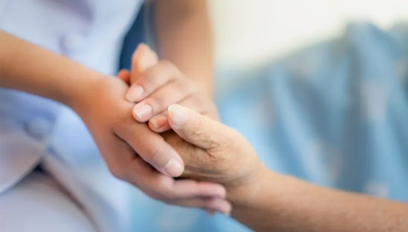 Eine Pflegekraft hält behutsam die Hand einer älteren Dame